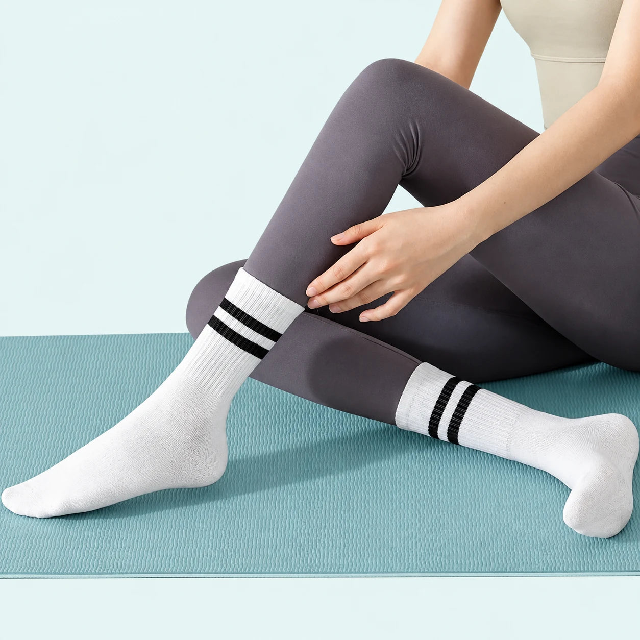 Woman seated on an exercise mat wearing white crew socks with black stripes
